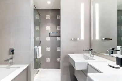 a white bathroom with two sinks and a shower at EDEN'S Homes & Villas - Atria Residences in Dubai
