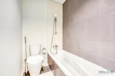 a white bathroom with a toilet and a bath tub at Extensive 3BR Townhouse at Janusia Damac Hills 2 by Deluxe Holiday Homes in Dubai