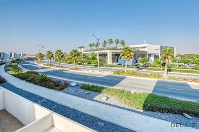 a road in front of a building with palm trees at Extensive 3BR Townhouse at Janusia Damac Hills 2 by Deluxe Holiday Homes in Dubai