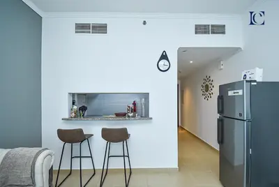 a kitchen with two bar stools and a refrigerator at Luxury Escapes - Lake View Brand New Studio in X1 Tower JLT in Dubai