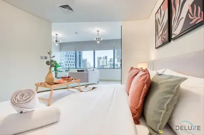 a bedroom with a white bed and a living room at Charming Studio at Sky Gardens DIFC by Deluxe Holiday Homes in Dubai