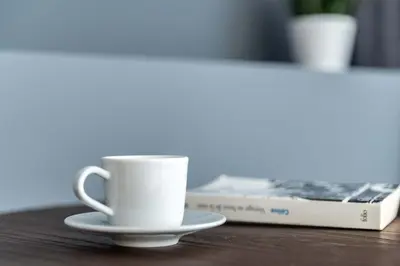 a white coffee cup sitting on a table next to a book at Silkhaus comfy furnished studio in the heart of DIFC in Dubai