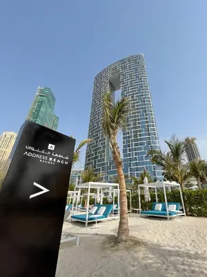 a building on the beach with chairs and a palm tree at The Smart Concierge - Address JBR in Dubai