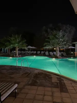 a swimming pool at night with a bench and palm trees at Big studio, Dubai SportCity, parking included in Dubai