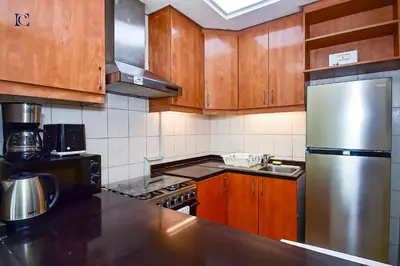 a kitchen with wooden cabinets and a stainless steel refrigerator at Luxury Escapes - Tranquil Retreat - Studio Apts near Metro and Mall - Discovery Gardens - SHAR & MCL in Dubai