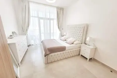 a white bedroom with a bed and a window at Modern 1BR in Jumeirah Village Circle (Pool View) in Dubai