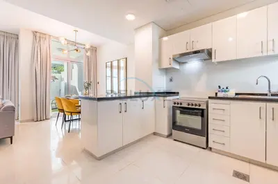 an open kitchen with white cabinets and a dining room at Furnished 3-Bedroom Townhouse, Just Minutes Drive from Al Marmoom Heritage Village and Popular Dubai Attractions, Albizia, Damac Hills 2 by Deluxe Holiday Homes in Dubai