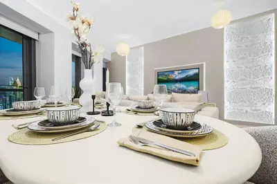 a white dining room with a table with plates and wine glasses at Luxury 2BR with Skyline and Sea Views, Near Burj Khalifa & Dubai Mall in Dubai