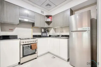 a kitchen with white cabinets and a stainless steel refrigerator at Whimsical 2BR at Bella Rose Barsha South by Deluxe Holiday Homes in Dubai