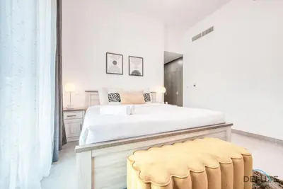 a bedroom with a white bed and a yellow stool at Whimsical 2BR at Bella Rose Barsha South by Deluxe Holiday Homes in Dubai