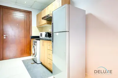 a stainless steel refrigerator in a kitchen with wooden cabinets at Serene Studio in Elite Residences 4 Sports City by Deluxe Holiday Homes in Dubai