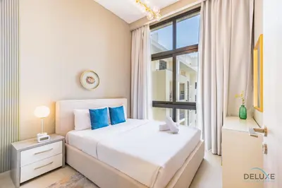 a bedroom with a bed with blue pillows and a window at Charming 2BR at Rawda Parkview Town Square Dubailand by Deluxe Holiday Homes in Dubai
