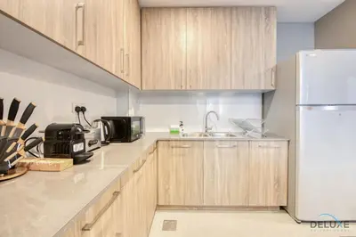 a kitchen with wooden cabinets and a white refrigerator at Charming 2BR at Rawda Parkview Town Square Dubailand by Deluxe Holiday Homes in Dubai
