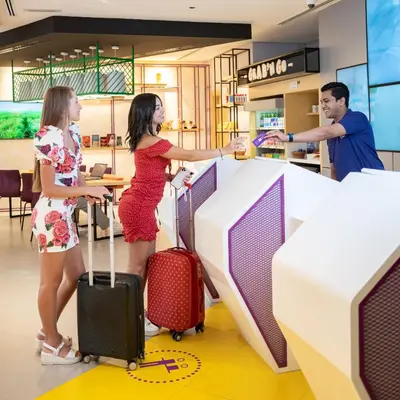 two women standing at a counter with luggage at Studio M Al Barsha Hotel by Millennium in Dubai