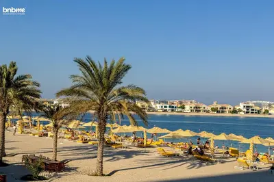 a beach with chairs and umbrellas and the water at bnbme - Beachfront 1BR Palm Jumeirah Apt w Balcony Sea Views Pool & Beach Access in Dubai