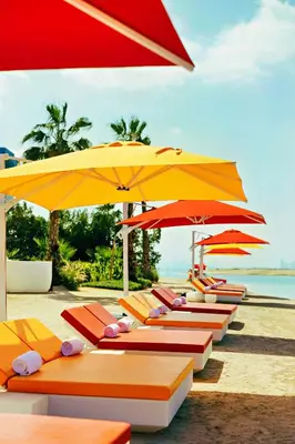 a row of lounge chairs with umbrellas on a beach at Voco Dubai Monaco, The Heart of Europe by IHG-Adult only in Dubai