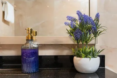 a bottle of purple liquid next to a vase with purple flowers at White Sage - Elite Residence 1 bedroom in Dubai