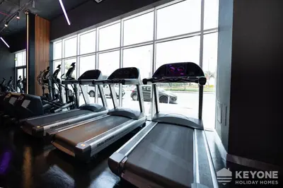 a row of treadmills in a gym with large windows at Modern & Stylish Studio in JVT in Dubai