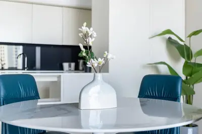 a white kitchen with a table with a vase with flowers at Silkhaus contemporary 1BDR with Downtown view in DIFC in Dubai