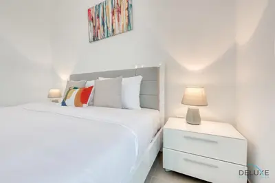 a white bedroom with a bed and a nightstand with a lamp at Fancy 2BR at Hayat Boulevard 2A Town Square By Deluxe Holiday Home in Dubai
