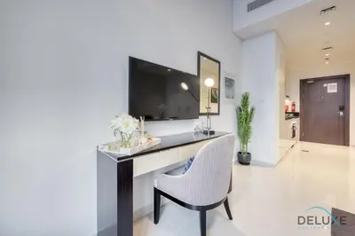 a room with a desk with a chair and a television at Sunlit Studio at Golf Promenade 2A DAMAC Hills By Deluxe Holiday Homes in Dubai