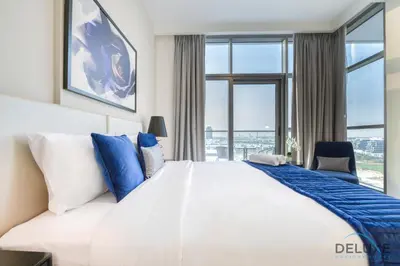 a bedroom with a large white bed with blue pillows at Sunlit Studio at Golf Promenade 2A DAMAC Hills By Deluxe Holiday Homes in Dubai