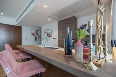 a kitchen with a large wooden counter with pink chairs at Luxury 2BD apartment in MarinaGate Jumeirah Living in Dubai
