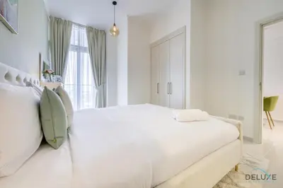 a white bedroom with a large white bed and a window at Prime 1BR at Carson B DAMAC Hills Dubailand by Deluxe Holiday Homes in Dubai