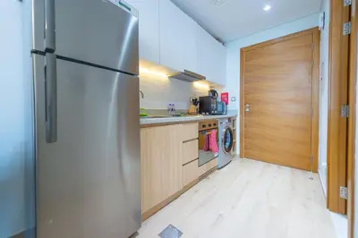 a kitchen with a stainless steel refrigerator and wooden cabinets at Luxury Escapes - Cozy Studio In front of Metro Stn - Access to Gym & Pool - Aura Azizi in Dubai