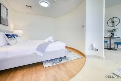 a white bedroom with a bed and a table at Best Value Modern 1BR with Pool & Stunning Views by Deluxe Holiday Homes in Dubai
