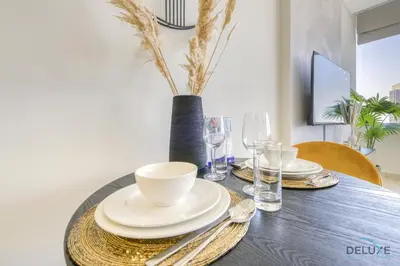 a dining room table with plates and glasses and a vase at Affordable Luxury Modern 1BR with Pool & Balcony by Deluxe Holiday Homes in Dubai