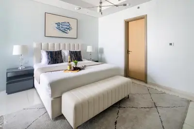 a white bedroom with a large bed and a stool at Frank Porter - Paramount Midtown in Dubai