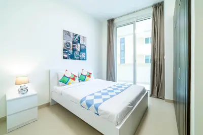 a white bedroom with a bed and a window at OYO 589 Najma Tower, Two bedrooms Apartments, Sports City in Dubai