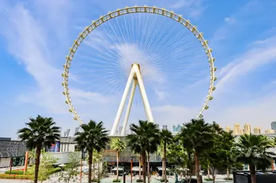 a large ferris wheel in a city with palm trees at Livbnb - Upgraded 2BR, Near Shopping & Dining Hubs in Dubai