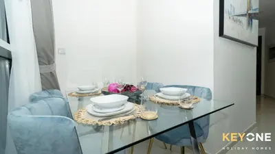 a dining room table with blue chairs and a glass table with dishes at Carson Elegant Living in One Bedroom in Dubai