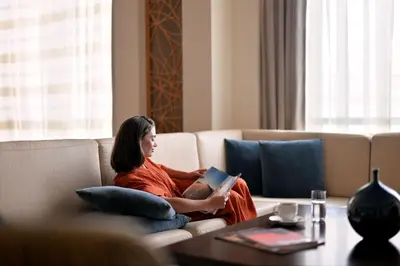 a woman sitting on a couch reading a book at Marriott Hotel Al Jaddaf, Dubai in Dubai