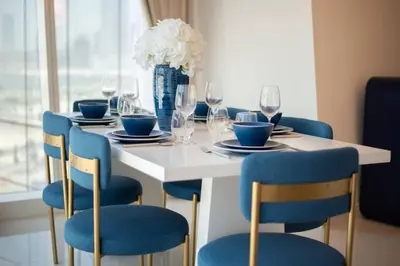 a white table with blue chairs and a vase with flowers at Blue dream apartment with Harbour view in Marina in Dubai