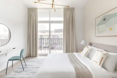 a white bedroom with a bed and a large window at Frank Porter - Belgravia 3 in Dubai