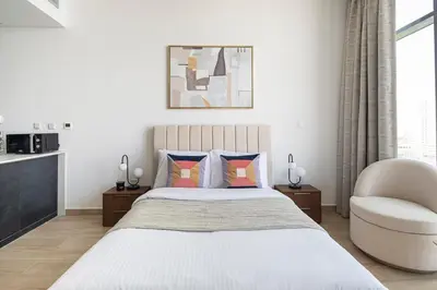 a white bedroom with a bed and a chair at Frank Porter - Regina Tower in Dubai