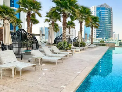 a pool with chaise lounge chairs and palm trees at HiGuests - Roomy and Chic Studio with Panoramic Canal Views in Dubai