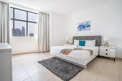 a white bedroom with a bed and a large window at RH- Modern Elegance 2BR, prime location, Walk to Dubai Mall in Dubai
