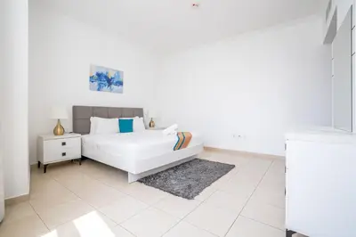 a white bedroom with a bed and a nightstand at RH- Modern Elegance 2BR, prime location, Walk to Dubai Mall in Dubai