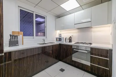 a kitchen with white counters and wooden cabinets at Hashtag Holiday Home - Excellent 1BDR with City View in Media city in Dubai