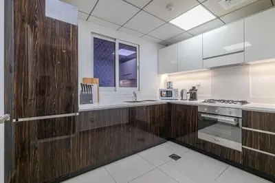 a large kitchen with white counters and wooden cabinets at Hashtag Holiday Home - Excellent 1BDR with City View in Media city in Dubai