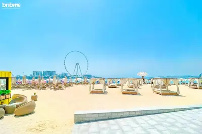 a beach with chairs and a ferris wheel in the background at bnbme - Luxury 1BR Marina View Apt w Balcony Pool Gym Access Near JBR Beach & Walk in Dubai