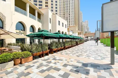 a sidewalk with umbrellas and potted plants and buildings at bnbme - Luxury 1BR Marina View Apt w Balcony Pool Gym Access Near JBR Beach & Walk in Dubai