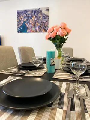 a table with black plates and a vase of pink roses at La Buena Vida Holiday Homes - Exquisite Spacious Luxe 1BR Apt , Full Marina View, Kitchen, 5 Min to Beach, JBR and Marina in Dubai