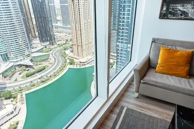 a couch in a room with a large window at Modern & Spacious 2-Bed Condo with Panoramic Lake Views, Dual Balconies, Steps from Dubai JLT Metro By 