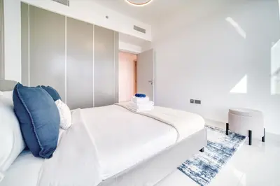 a white bedroom with a white bed with blue pillows at Emaar Beach Front 2BR with Sea & Marina Skyline Views in Dubai