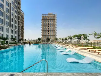 a swimming pool with white chairs and a tall building at GuestReady - Breath of Fresh Air in Dubai Hills in Dubai
